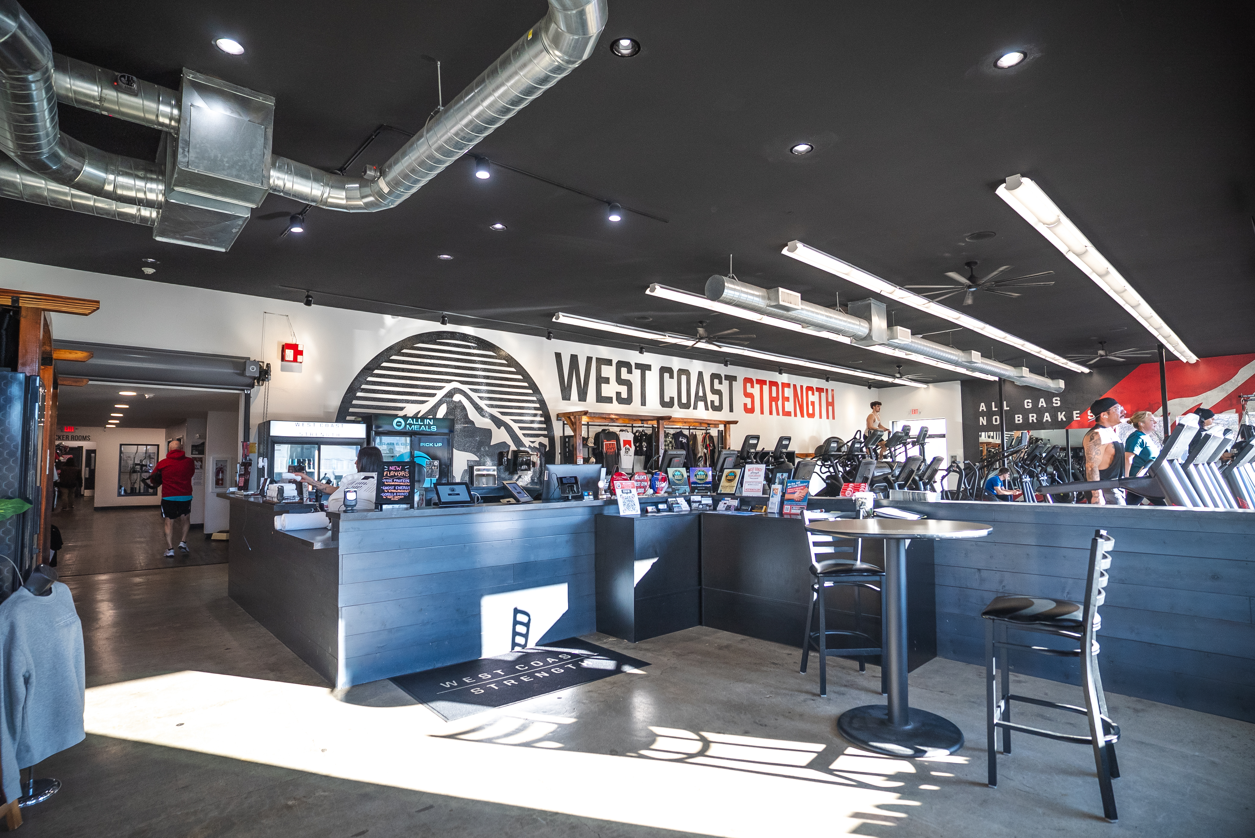 West Coast Strength front desk and lobby with the branded wall, check-in counter, and cardio area beyond