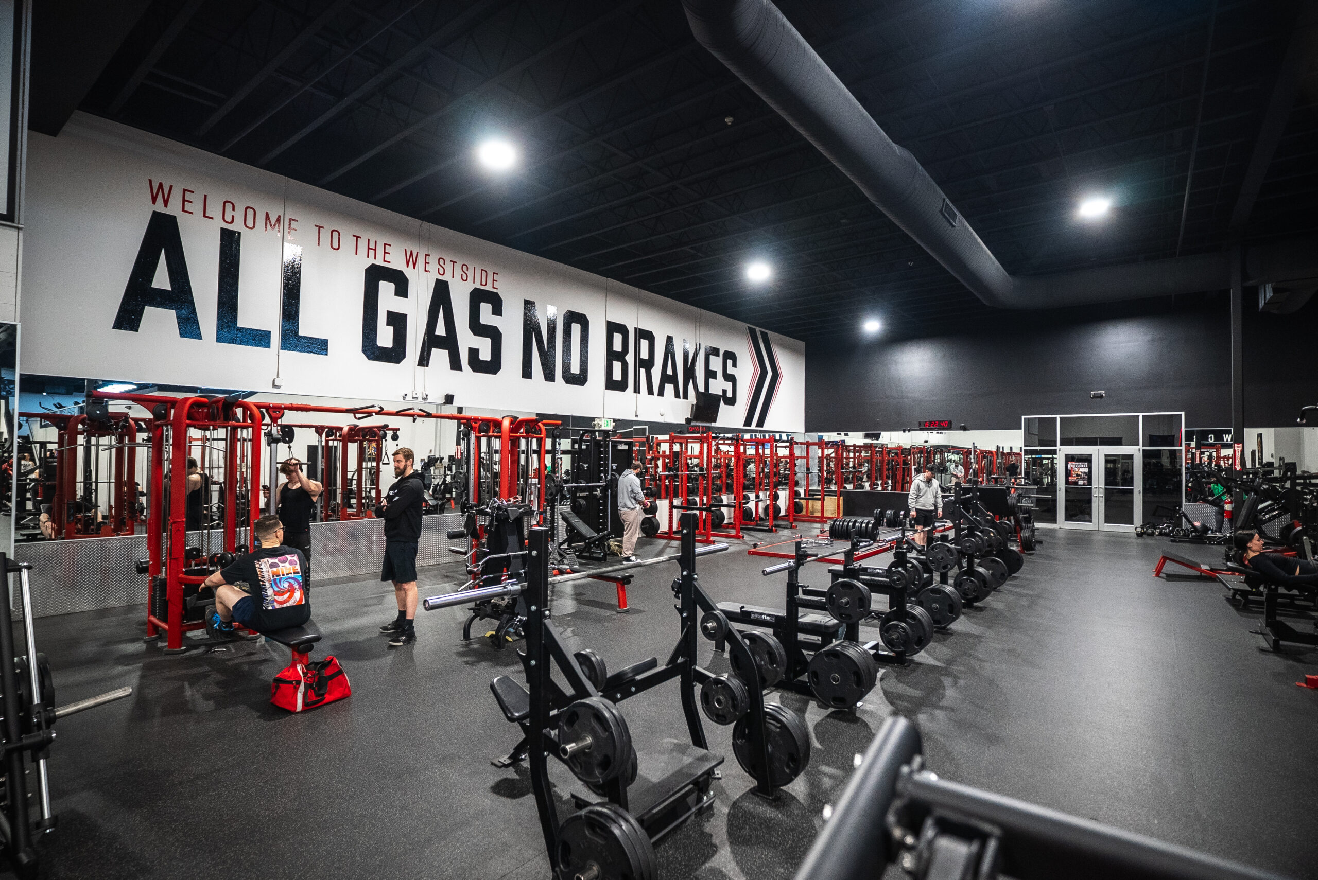 Members train among benches and red racks beneath the All Gas No Brakes wall mural