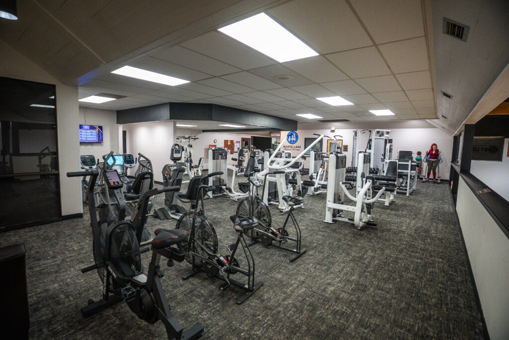 Cardio machines and strength equipment in a therapy area with a North Lake Physical Therapy sign