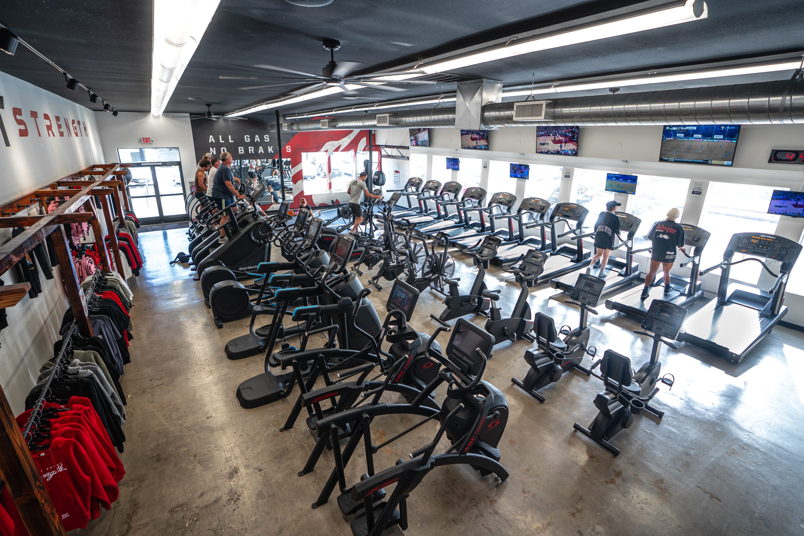Elevated view of the cardio area filled with treadmills, bikes, and ellipticals beside apparel racks and the All Gas No Brakes wall